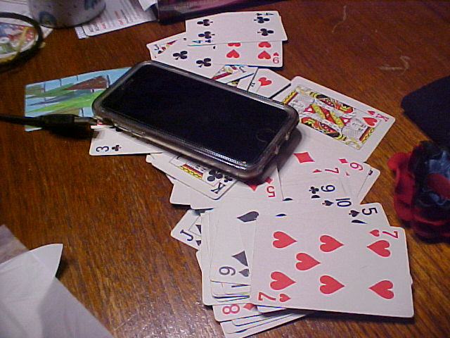 iPhone sitting on a pile of playing cards on a wood table.