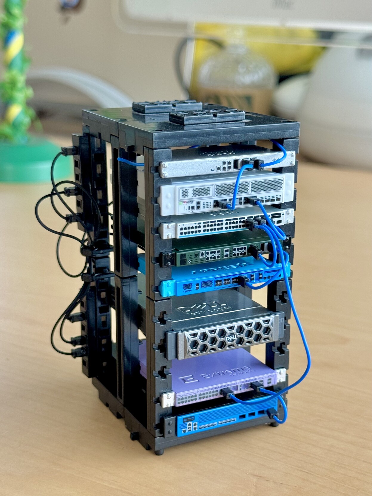 A little plastic toy network rack with a bunch of equipment from Cisco, Fortinet, Dell, Extreme network etc installed. Front view.