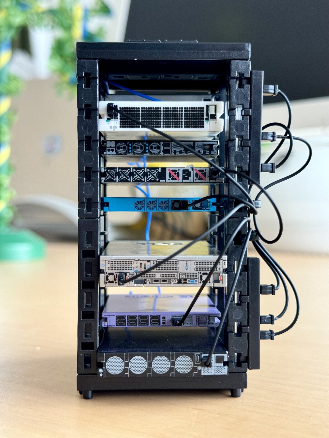 A little plastic toy network rack with a bunch of equipment from Cisco, Fortinet, Dell, Extreme network etc installed. Rear view showing the power distribution