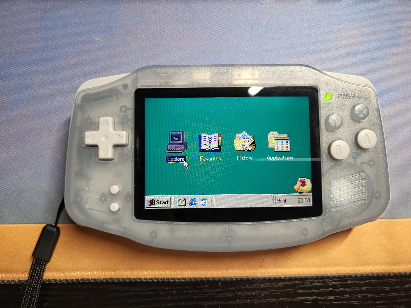 A Retro Handheld shaped like the original Game Boy Advance, displaying a screen that resembles the Windows 98 desktop, with four "desktop icons" representing the Explore, Favorite, History, and Applications buttons. The taskbar and start menu are at the bottom, and the old desktop sheep pet is at the bottom right.
