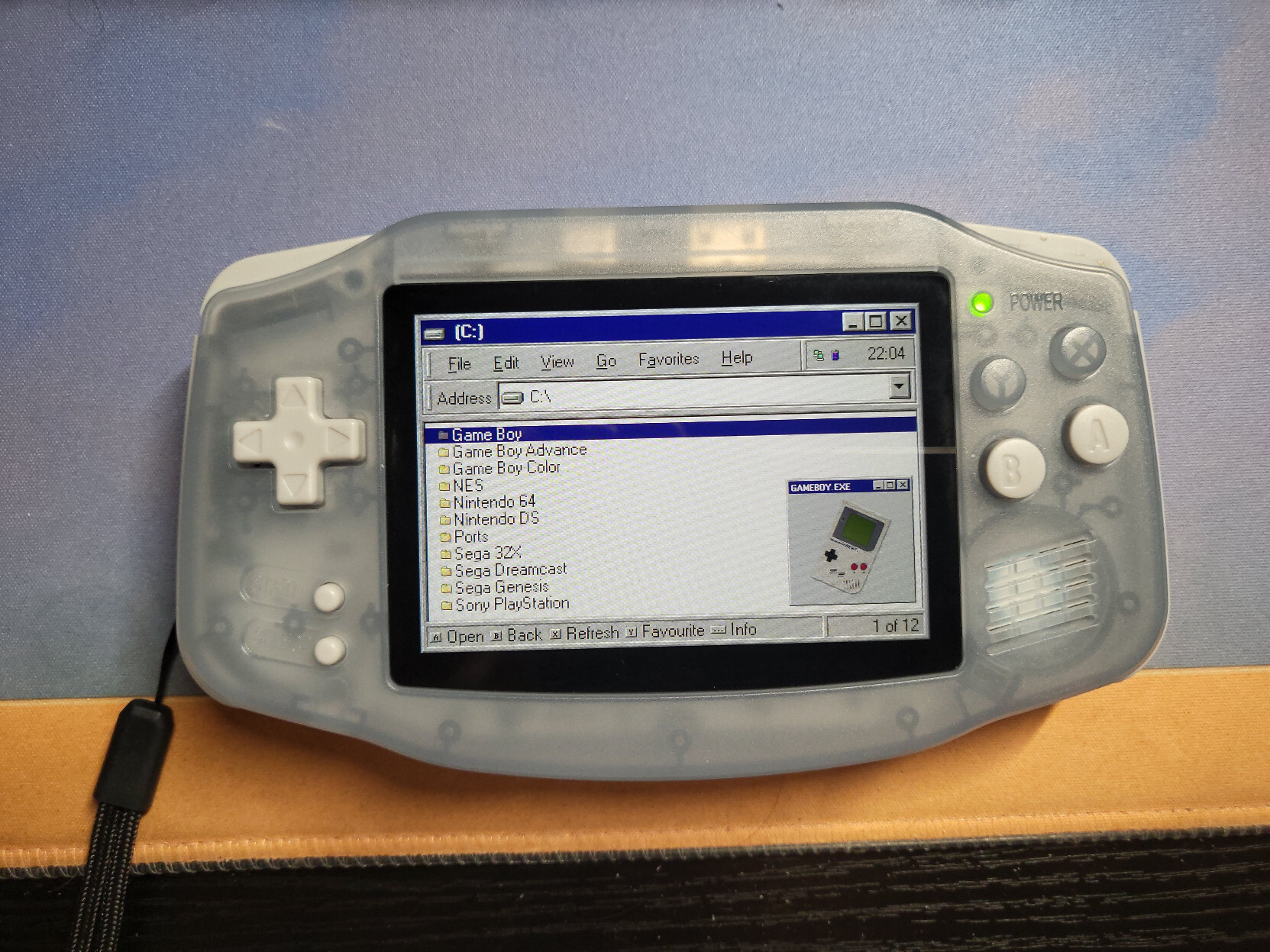 A Retro Handheld shaped like the original Game Boy Advance, displaying a screen that resembles the old File Explorer from Windows 98. It is displaying a list of systems, and the highlighted system (the original Game Boy) has a picture that looks like a pop up window.