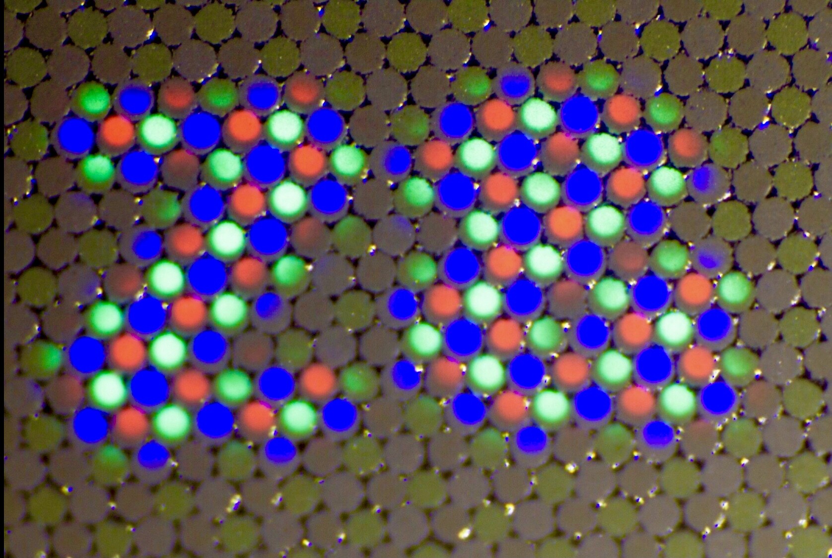 A close up macro photo of a commodore sx-64’s shadow mask crt showing individual red green and blue colour triplets lit up in the vague shape of a blurry letter Z and &. The letters appear white to the eye. The un-lit phosphor dots also show not being lit up, and  their colour is almost discernible too.