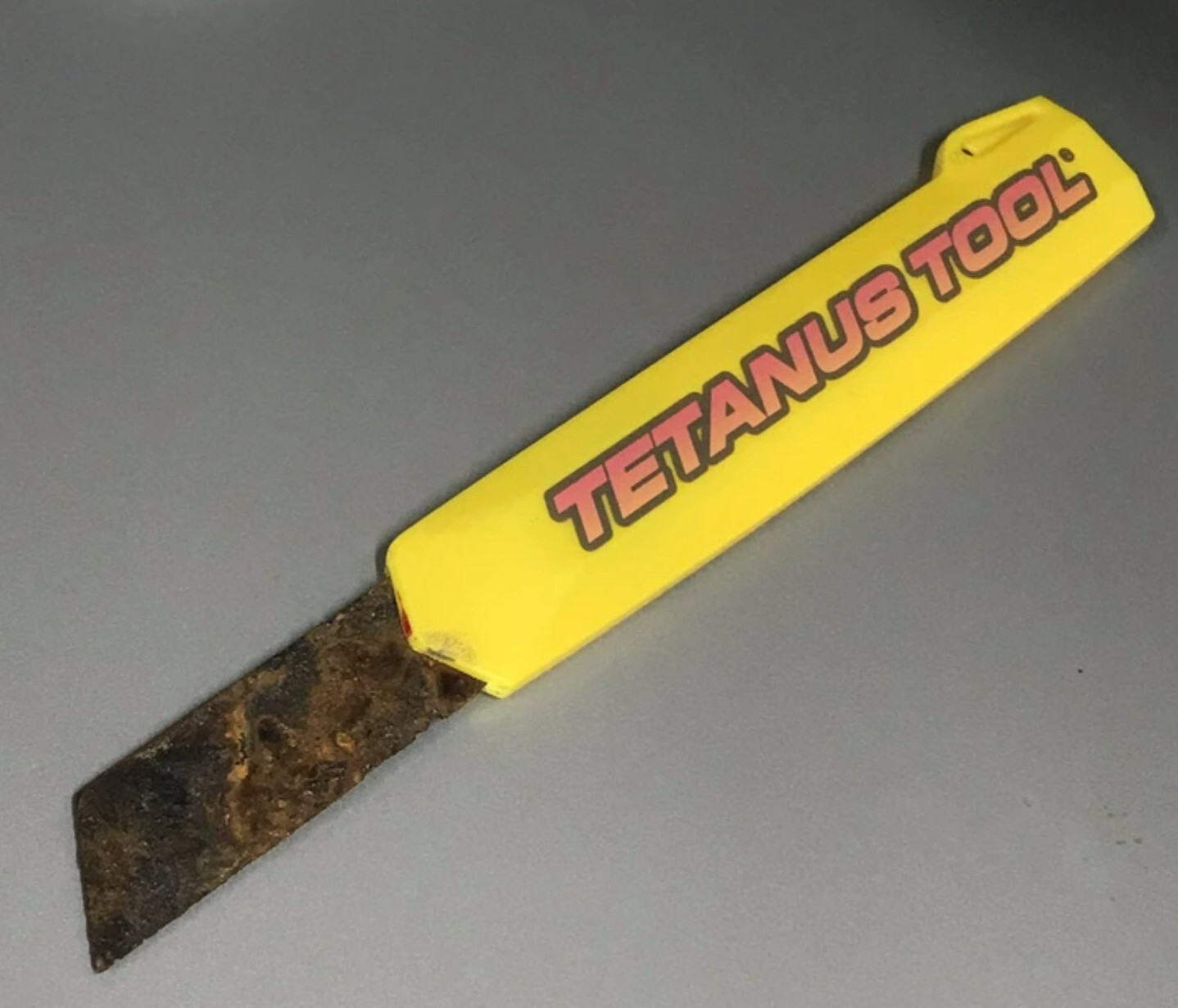 A photo of a yellow boxcutter with a heavily rusted blade with the branding TETANUS TOOL® along its plastic body.
