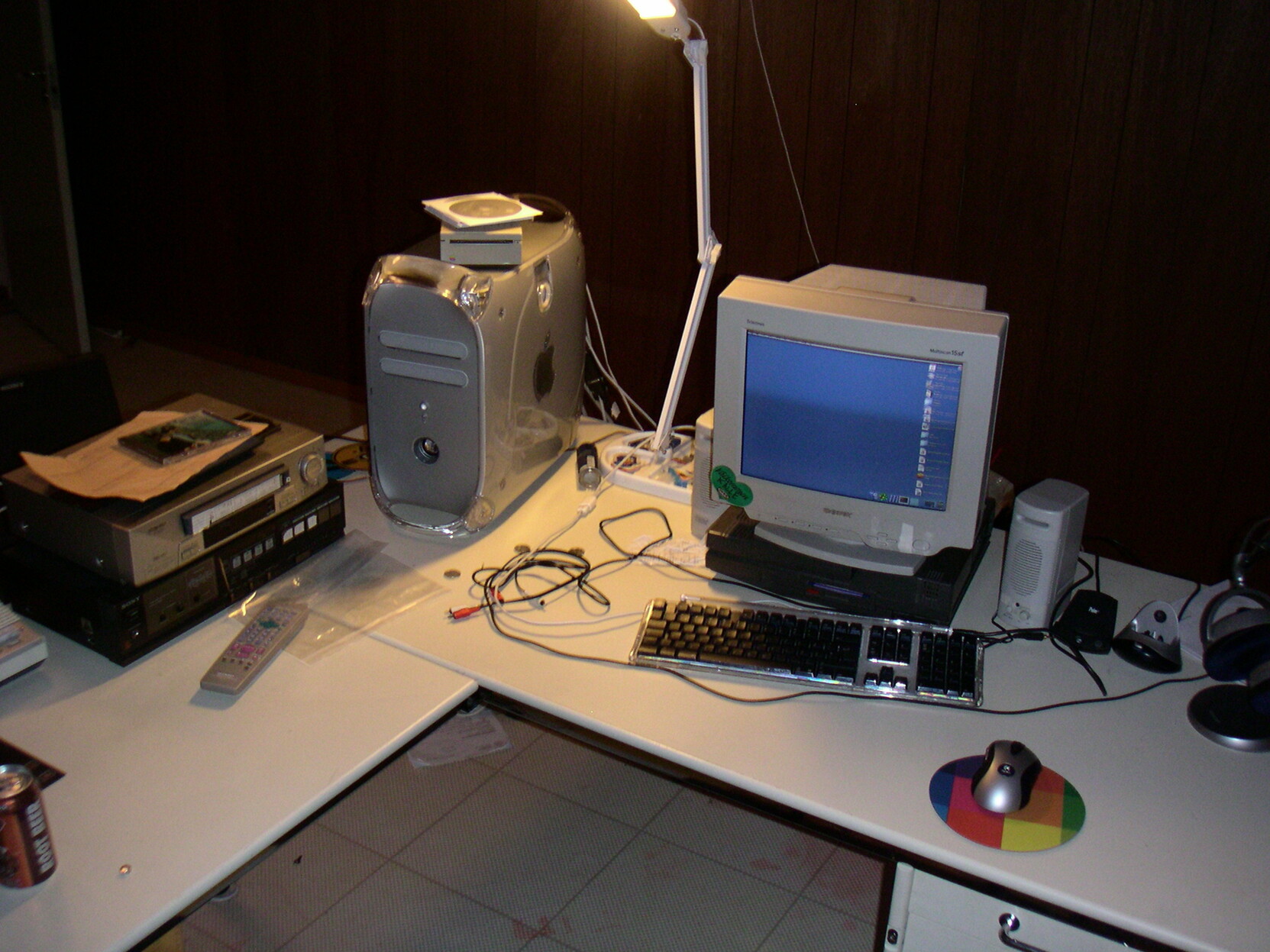 An L-shaped desk with a PowerMac G4 Quicksilver and a Sony Trinitron monitor standing on some Toshiba luggable. Also visible are Those PC Speakers Everyone Had, a Palm Vx dock, a Logitech MX700, a VHS deck, a 1980’s hifi amp with a large floor-standing speaking peaking out a corner. Also a root beer can.